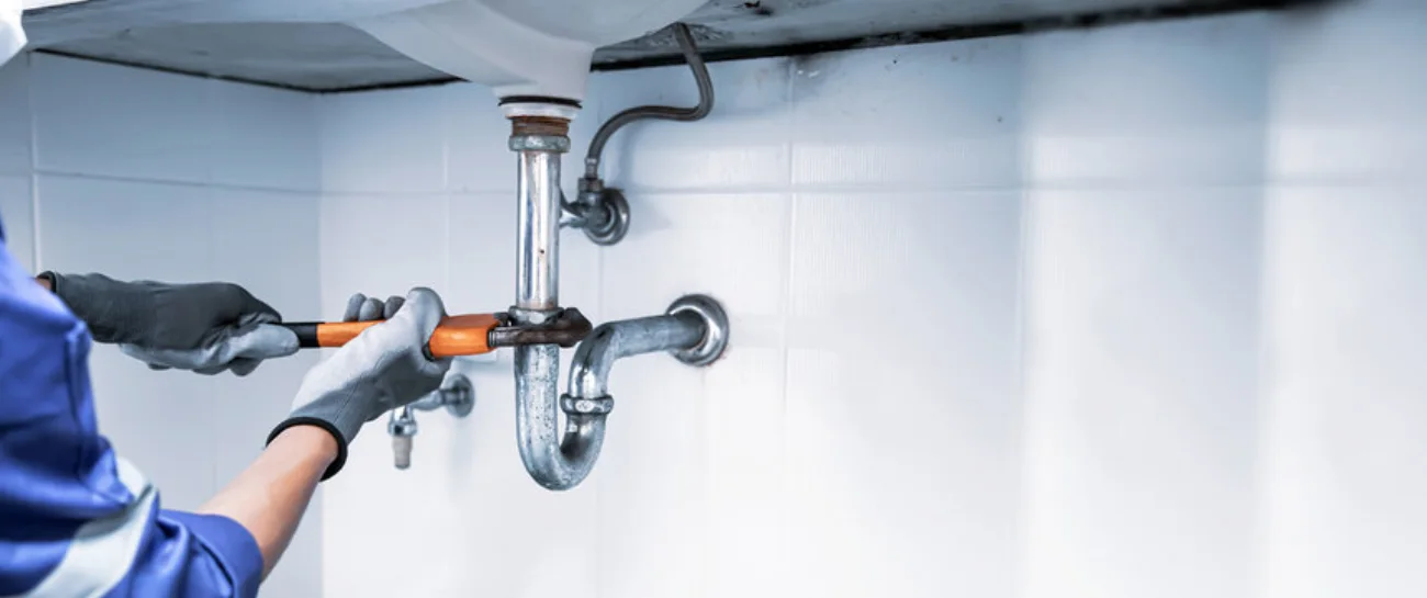 A plumber fitting pipework under a sink