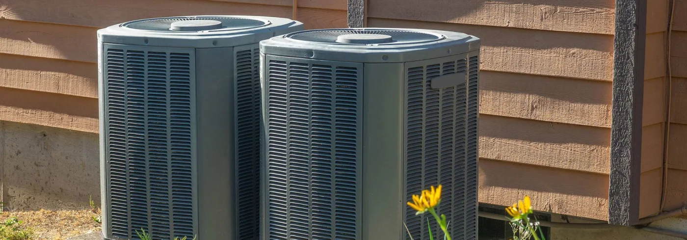 A pair of high-efficiency condenser units installed against a cedar-sided island home
