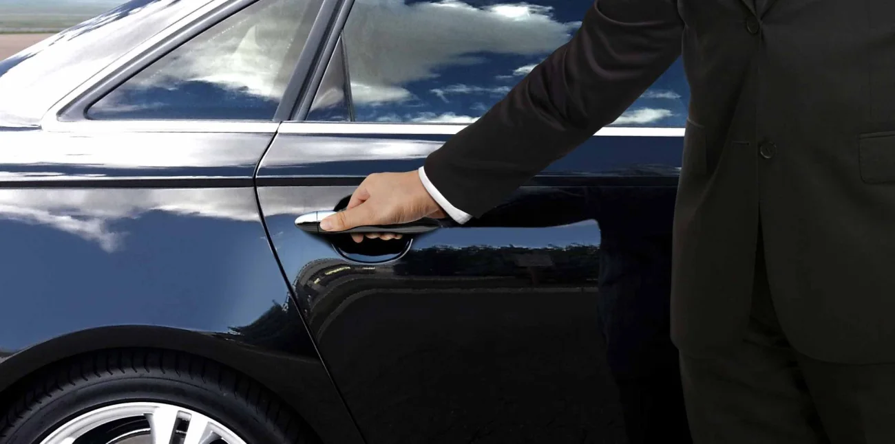 A driver opening the door of a sedan for a passenger